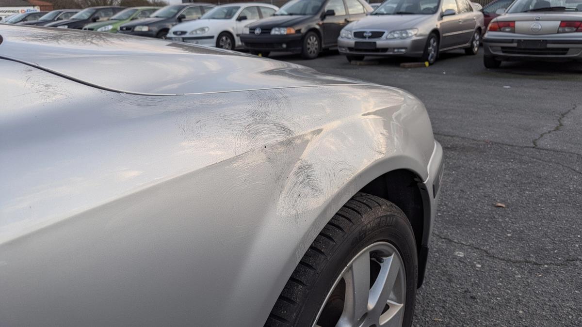 Repainted front fender of a used car with orange peel paint texture visible in raking light